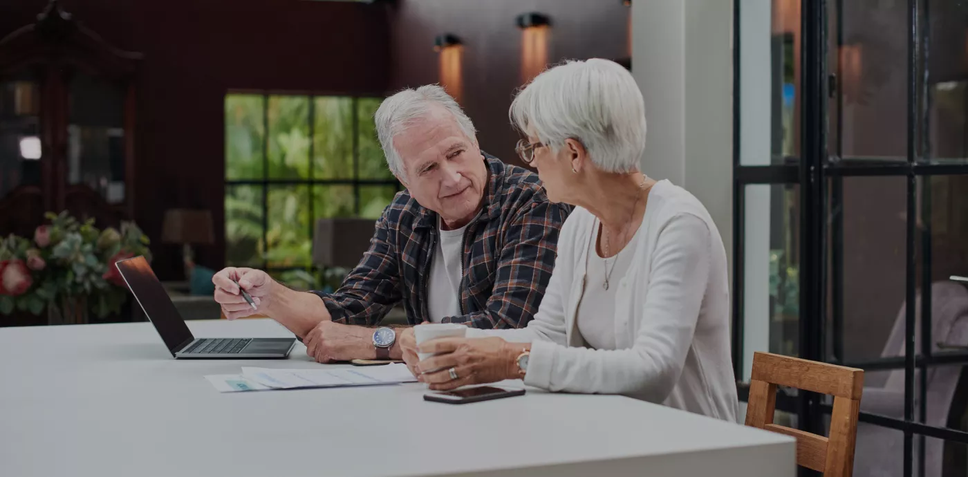 Older couple talking while looking over wealth management website at their kitchen counter