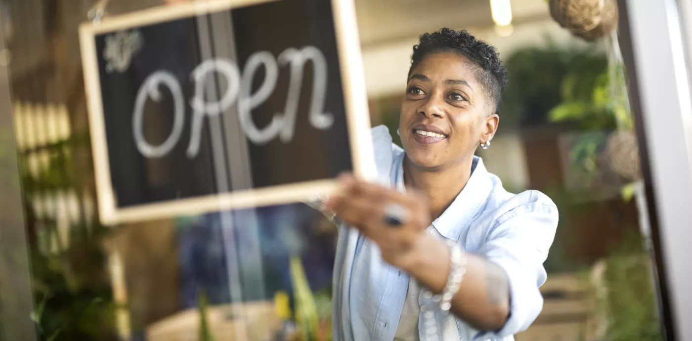woman putting up open sign in front of her business