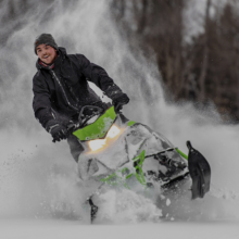man riding snowmobile through snow while smiling