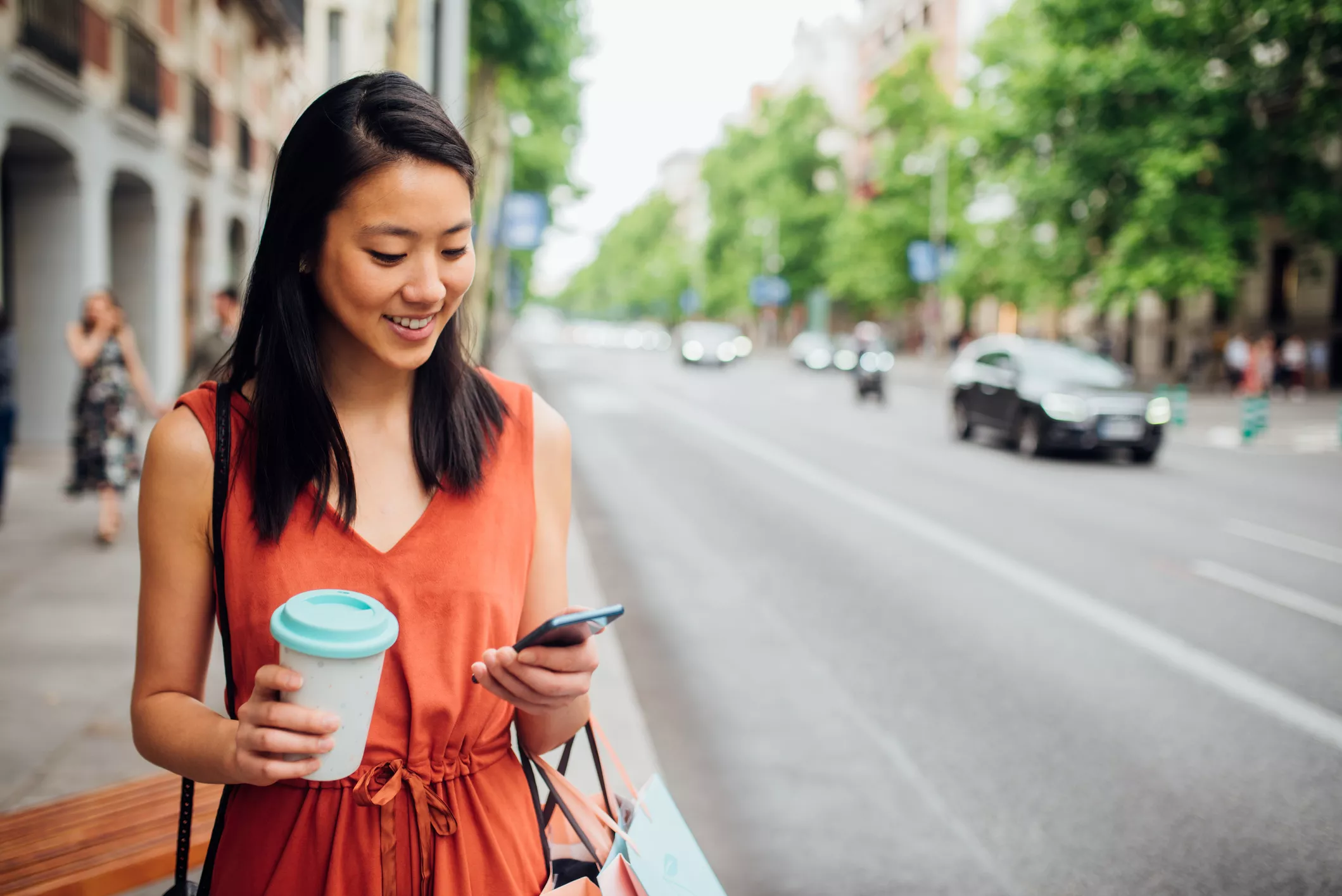 woman smiling while walking down street and looking at phone
