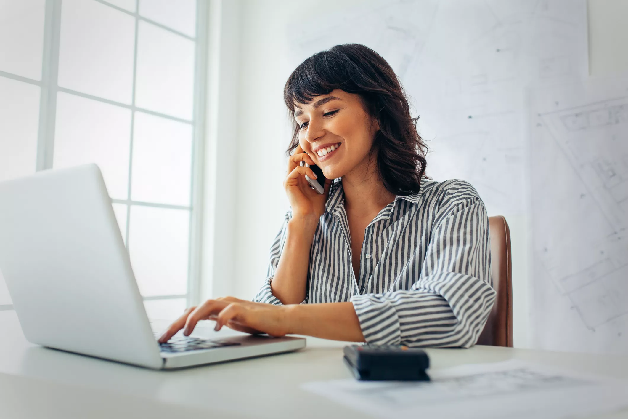 business woman smiling while she works on her computer and talk on the phone