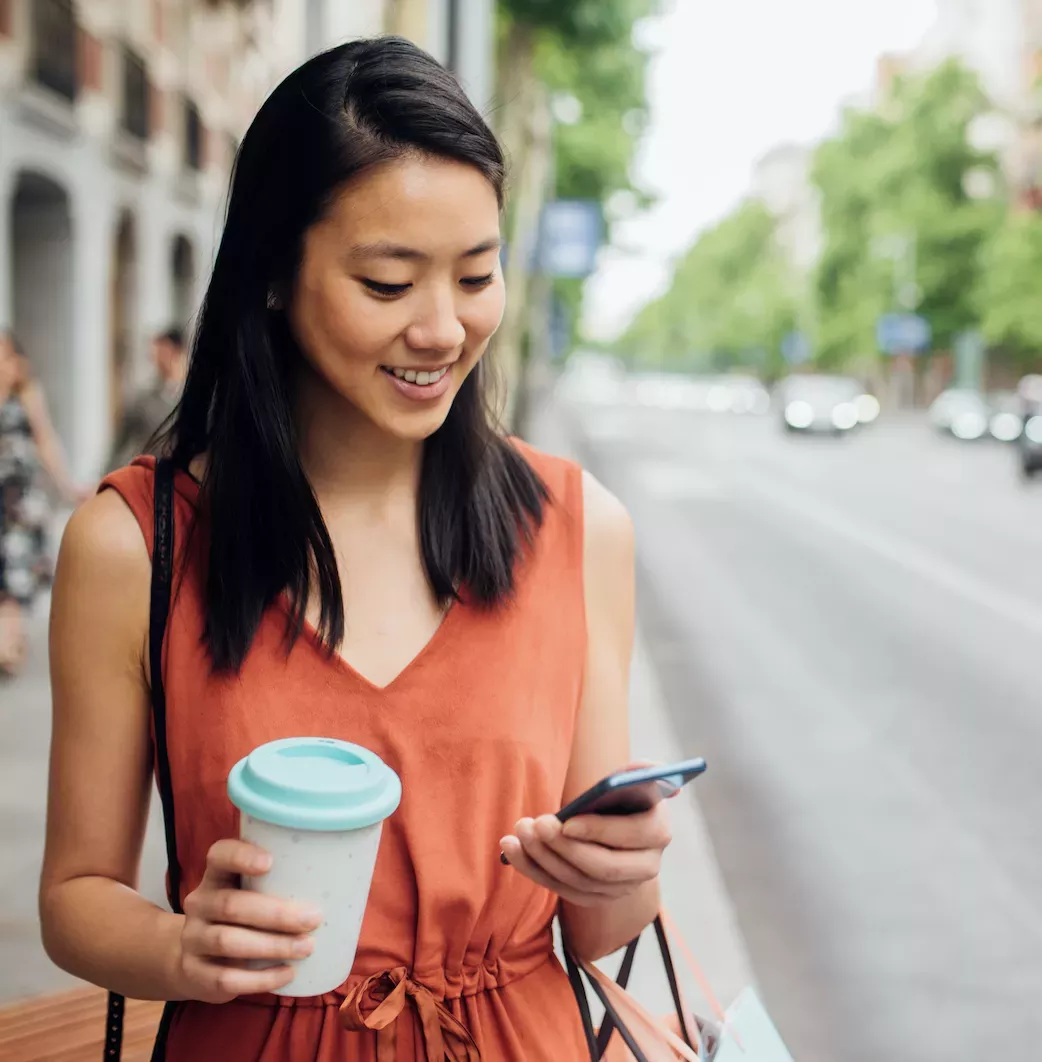 woman smiling while walking down the street and looking at phone