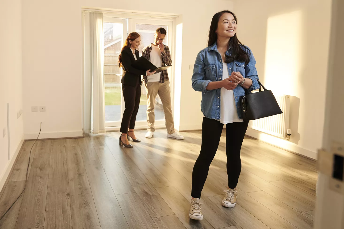 woman smiling as she looks at new rental with her husband and realtor talking in background